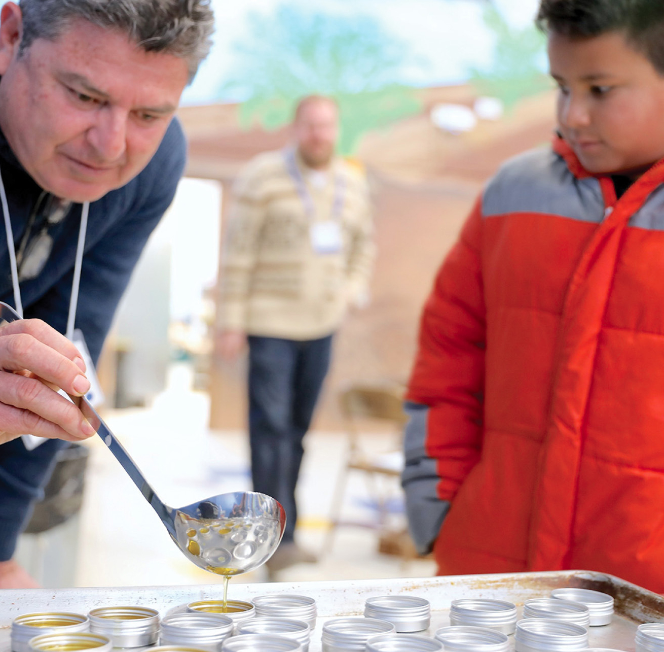 An educator carefully ladles liquid salve into a container.