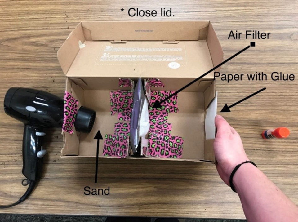 Figure 3 Testing apparatus made out of a shoebox, hairdryer, a place for the students’ prototype filter in the middle of the box, and a piece of graph paper coated with glue at the other end. 