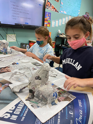 Students use a glue-water mixture to wet the newspaper strips they add to their armatures.
