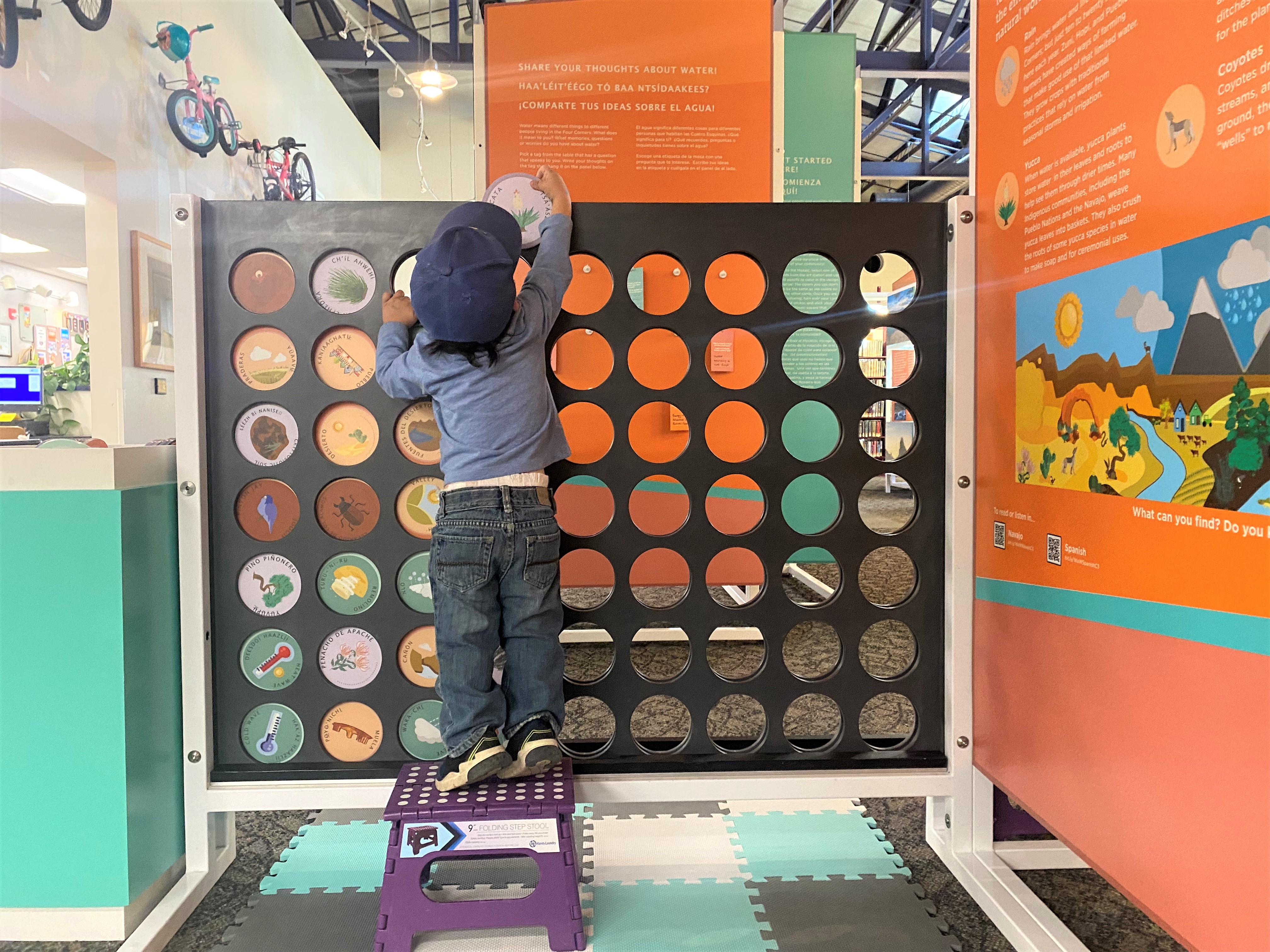 A young boy plays with the We are Water Connect Four interactive, which incorporates images of plants, animals, landscape features, and weather events from the southwestern United States and four languages, Navajo, Spanish, Ute, and English. 