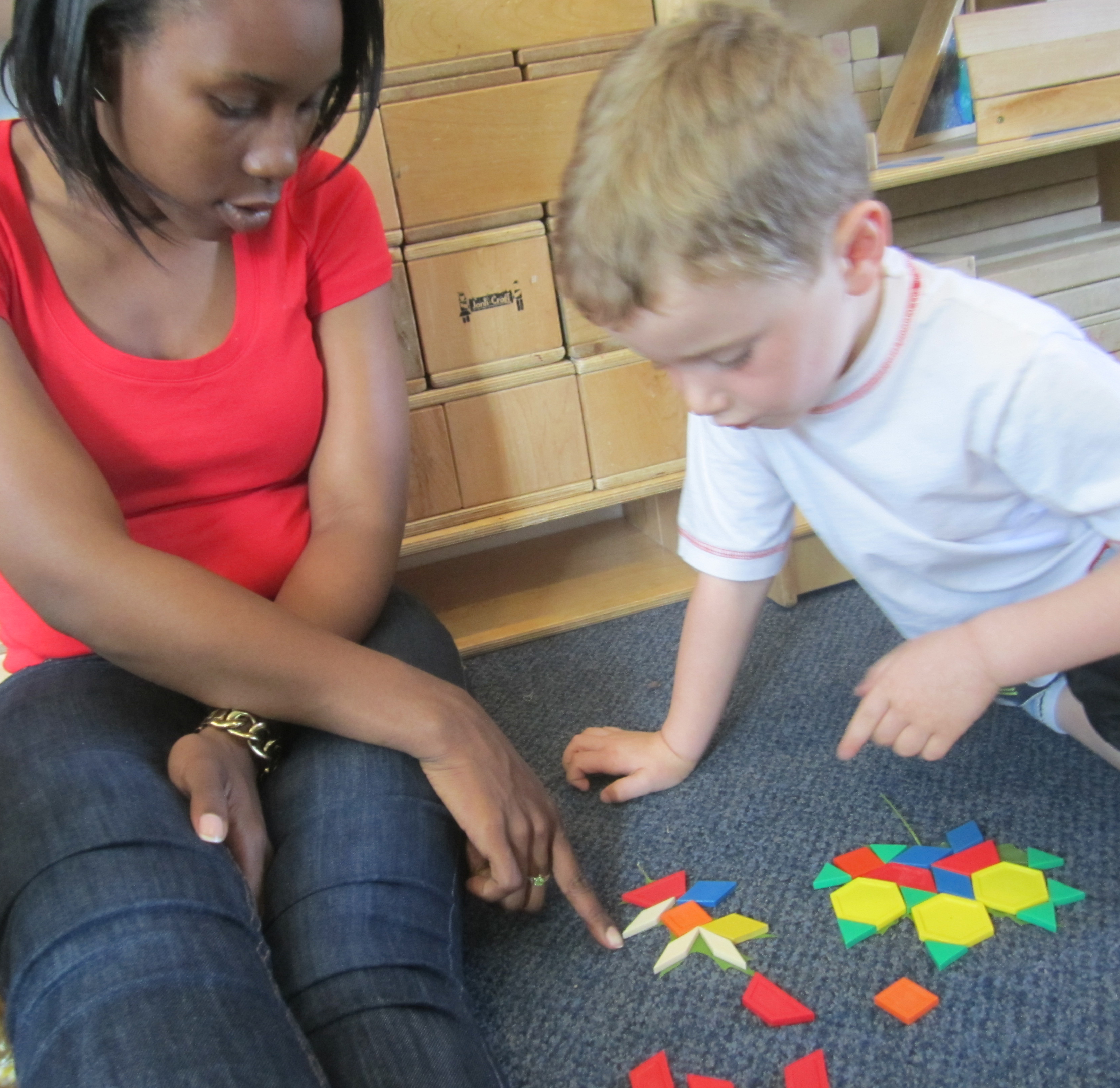 Teacher talks with child as they match pattern blocks to leaf shapes.