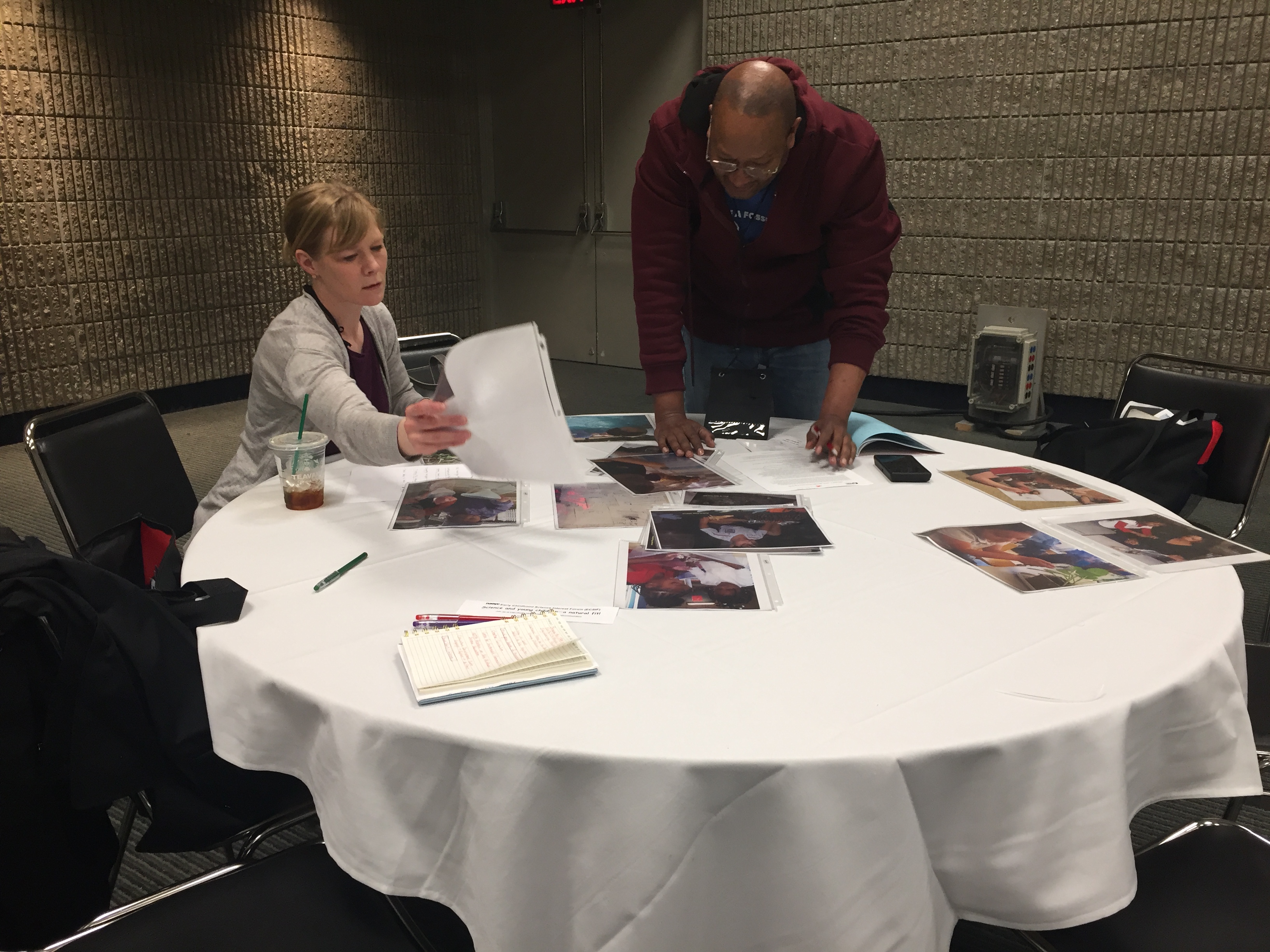 Two people stand at a table discussing photos.