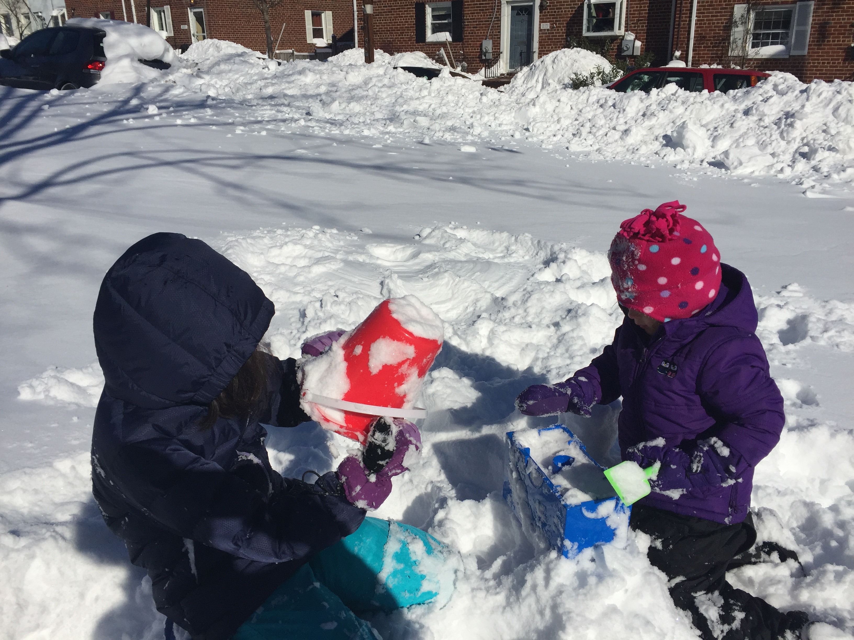 Two children playing in snow wearing snowsuits and hats.