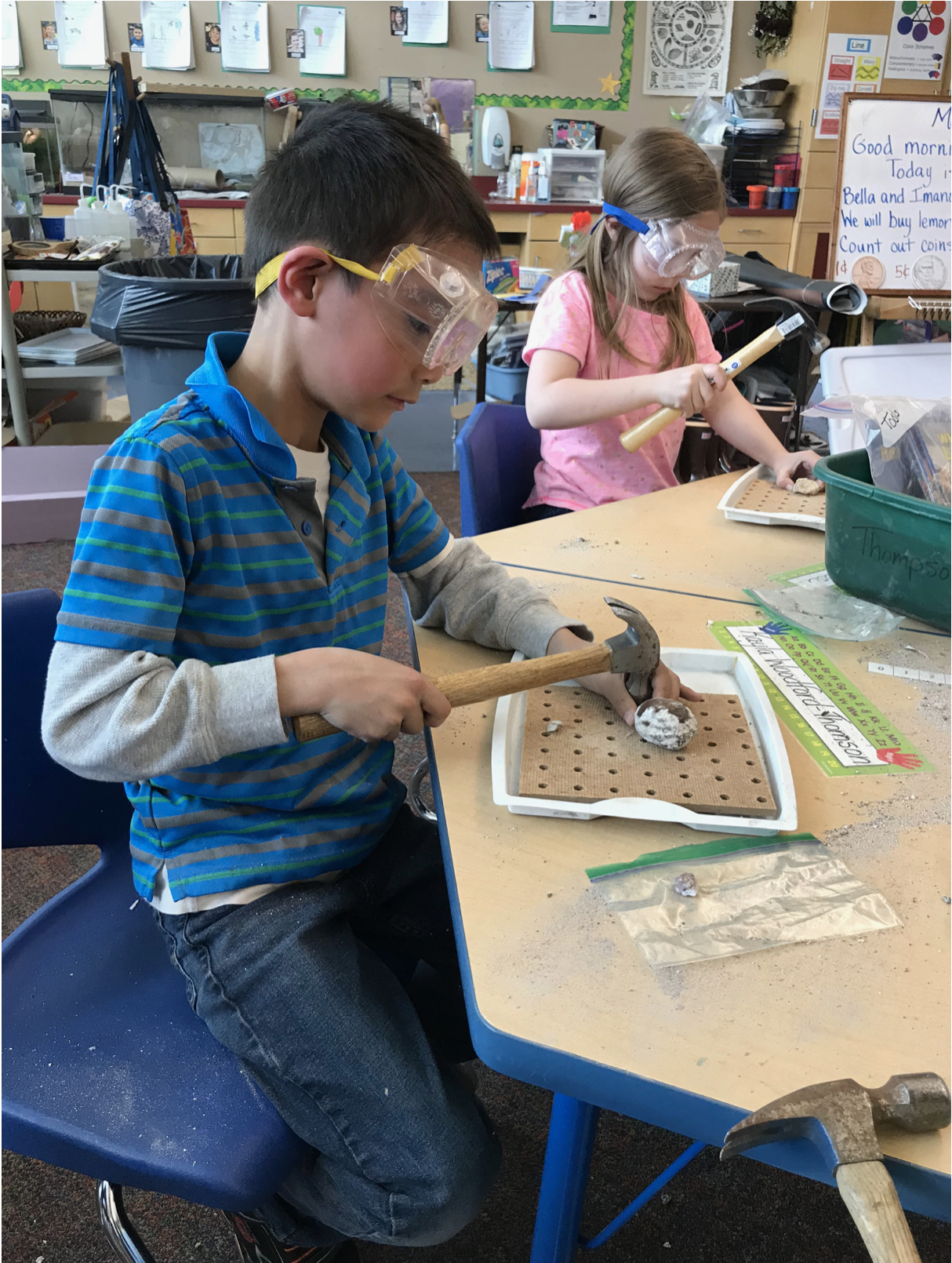 Elementary students wearing goggles using hammers to break open rock.