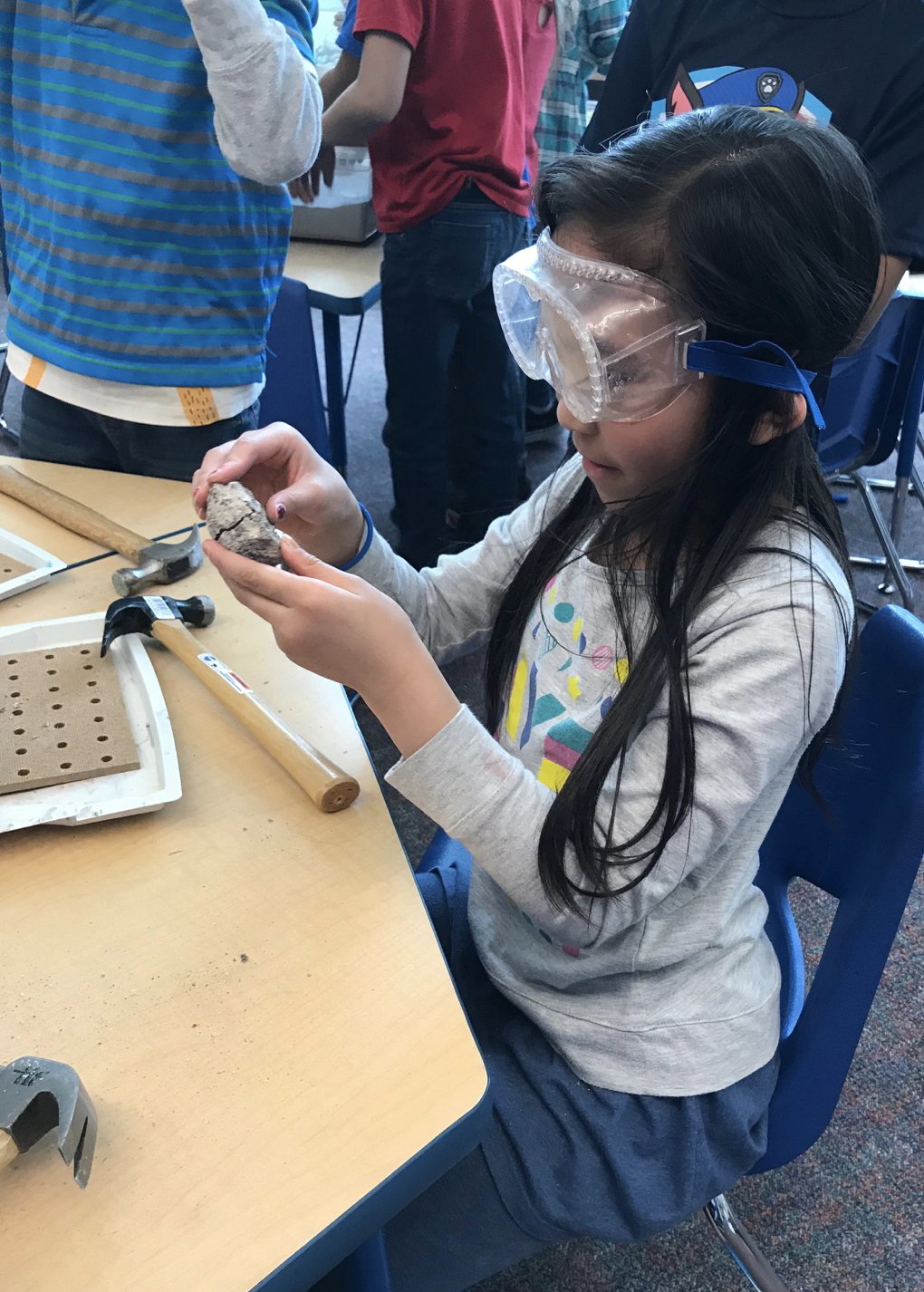 Elementary student wearing goggles using a hammer to open a rock.