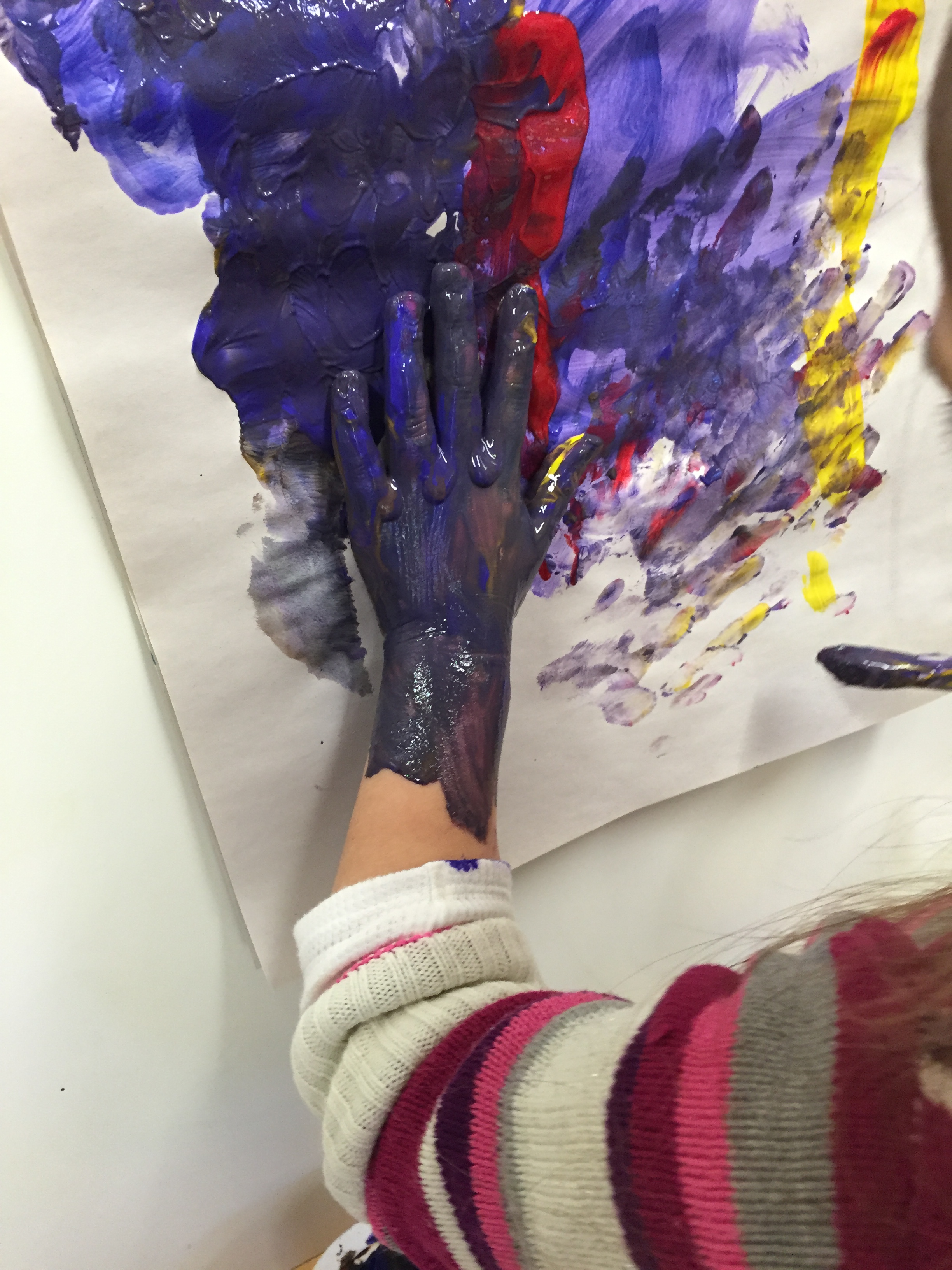 Child explores the feel of tempera paint at the easel.