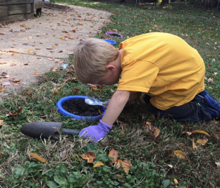 Child using magnifier to look at earthworms in soil.