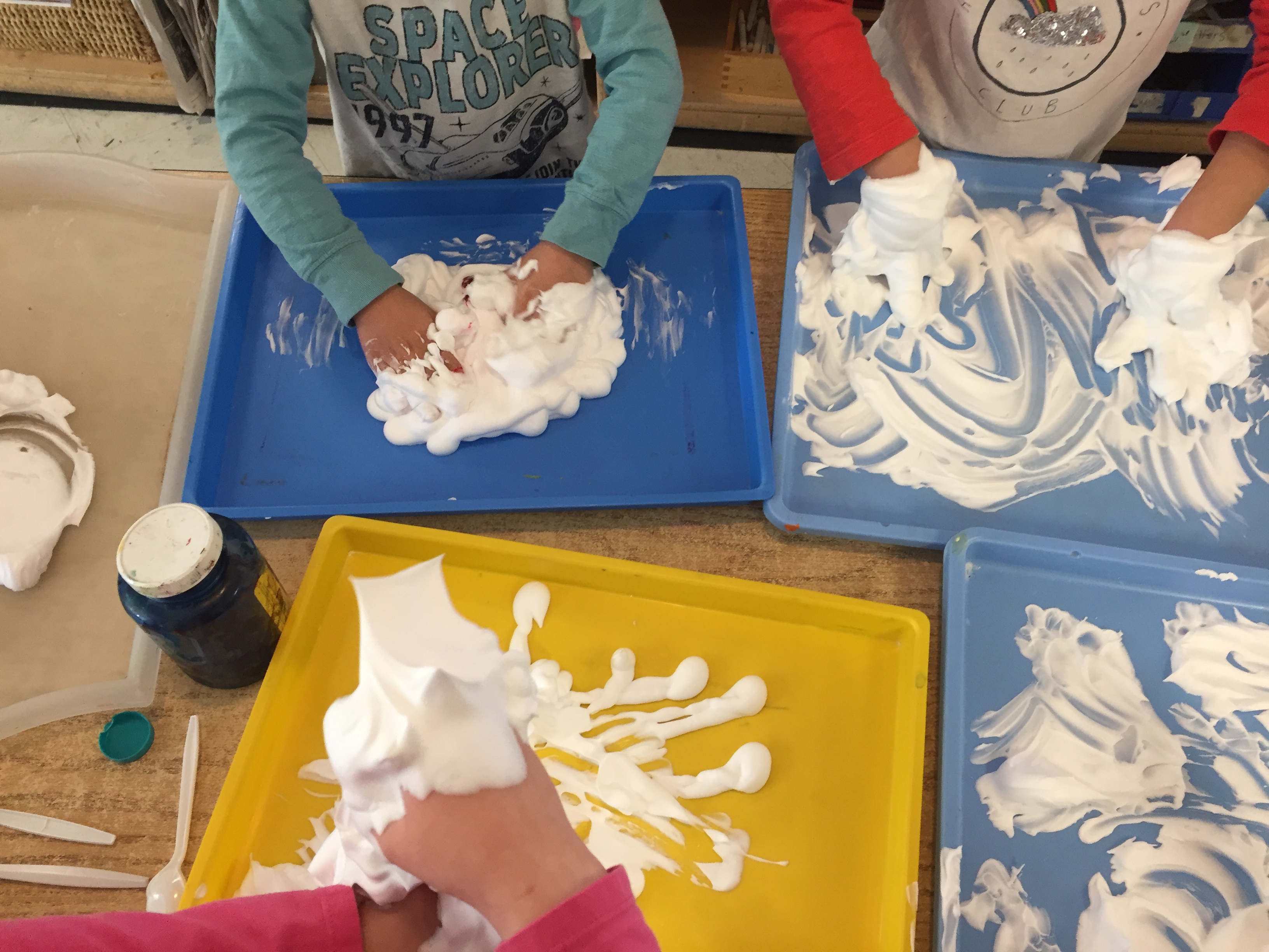 Children use shaving cream on trays as a sensory experience.