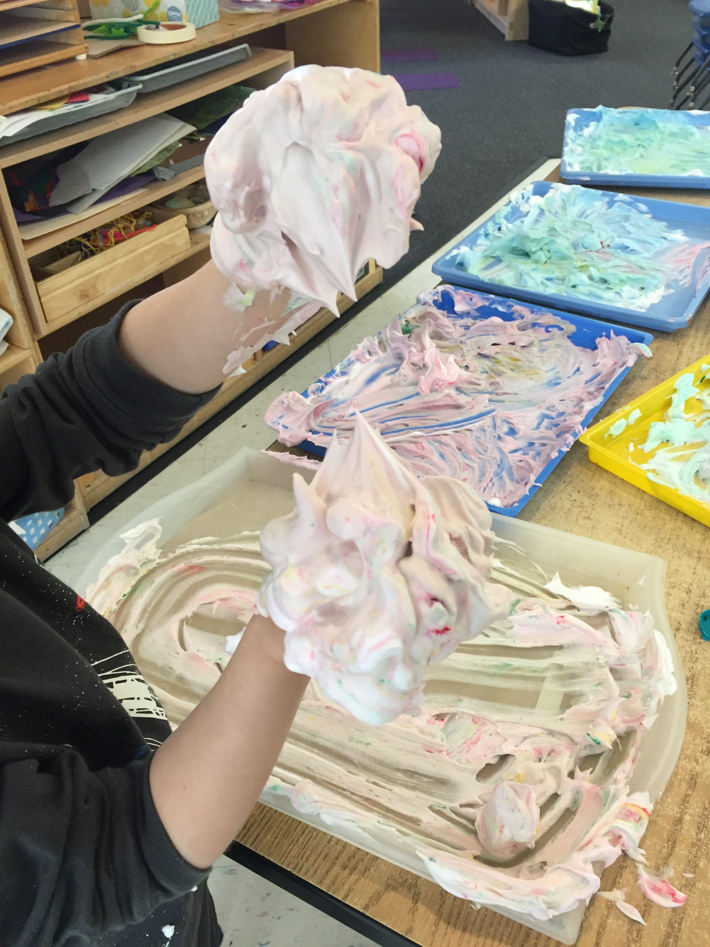 4 year old child holds up hands covered with shaving cream paint.