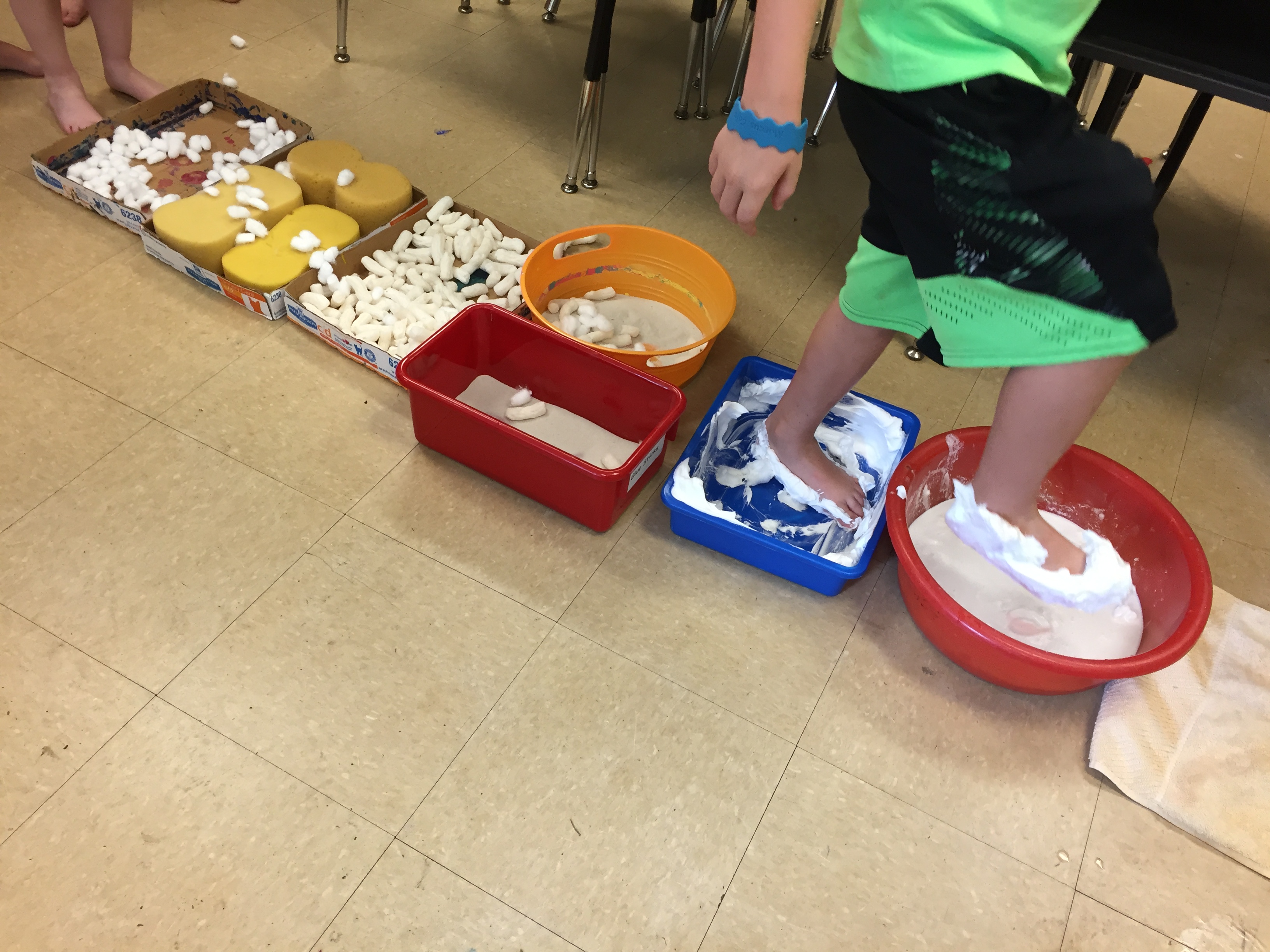 5 year old child walks through a series of trays holding different materials--a "sensory walk."
