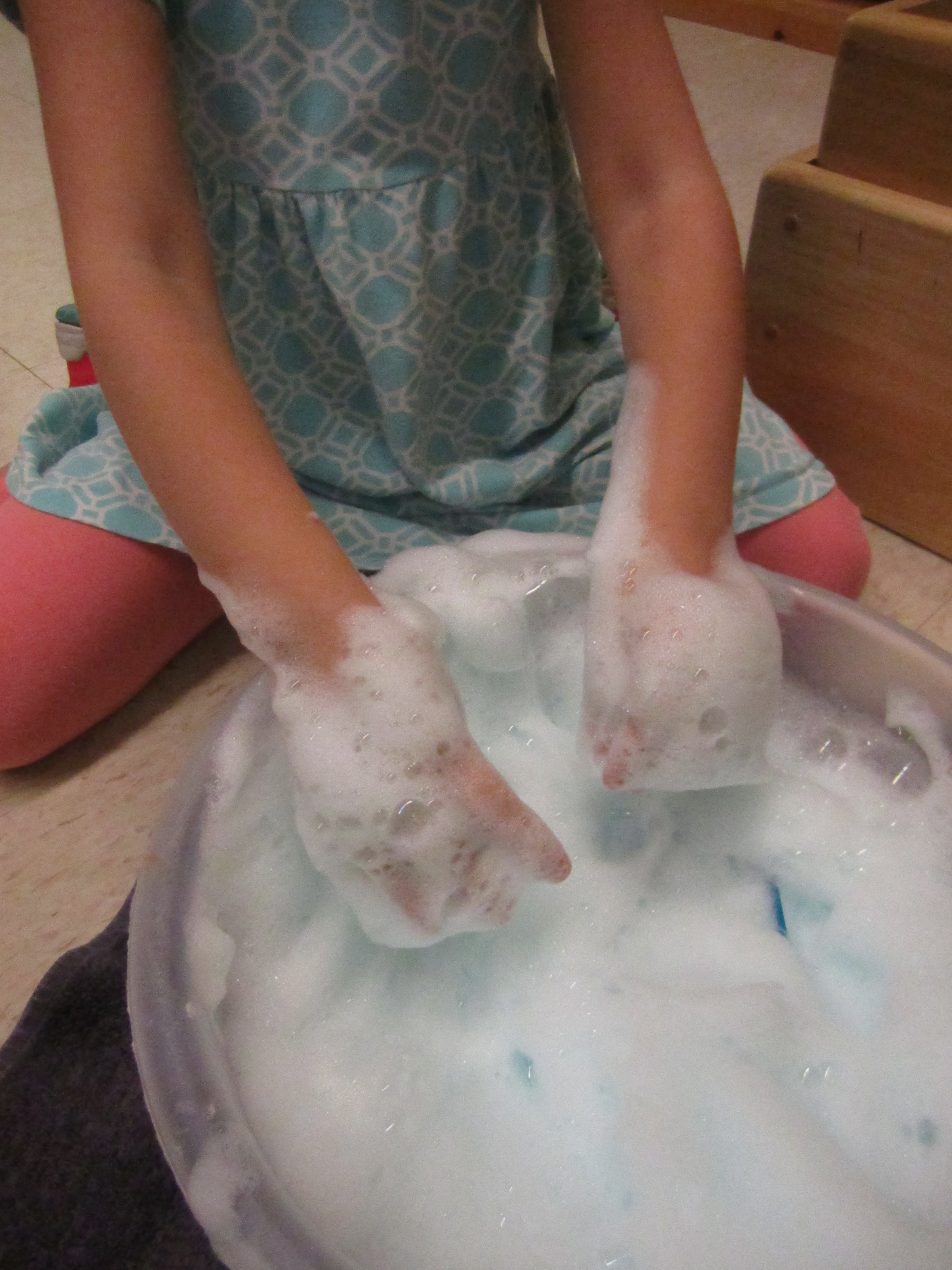 Child has two hands in a bowl of soap foam.