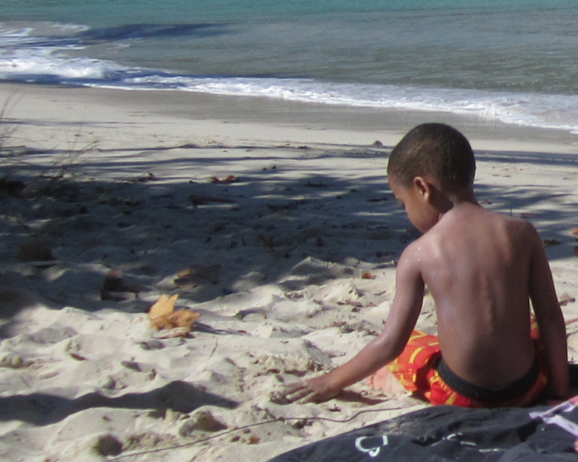 Child sits on a beach feeling sand.