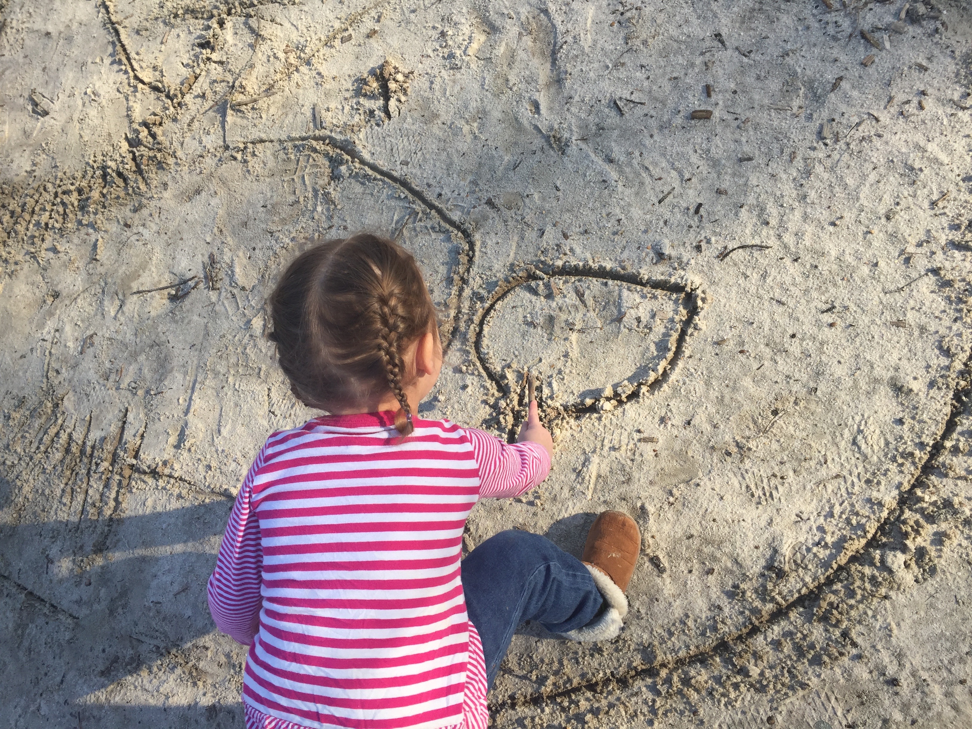 Child using a stick to draw in sand.