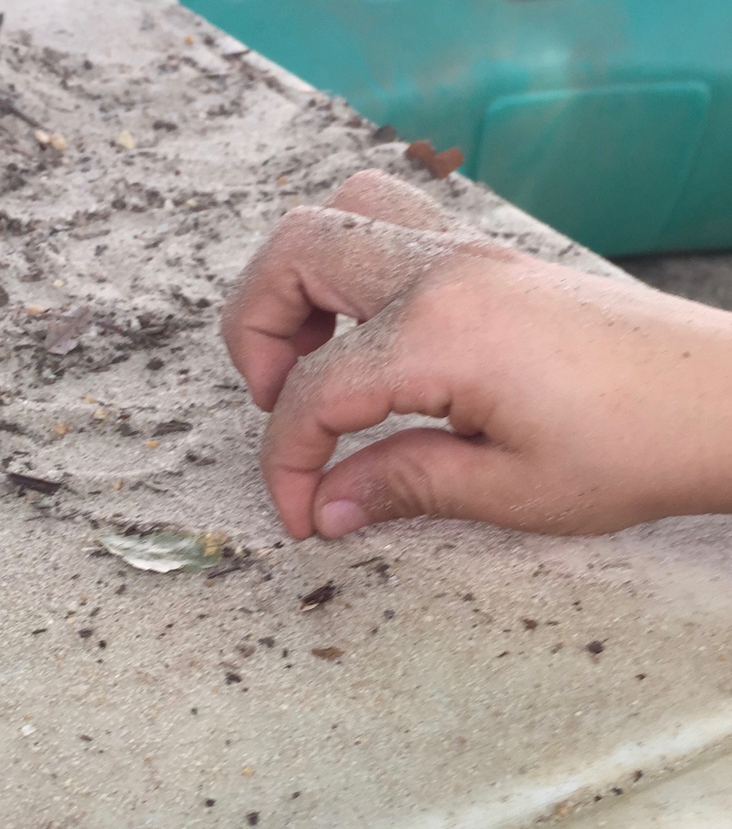 Child's hand pinching up dry sand grains.
