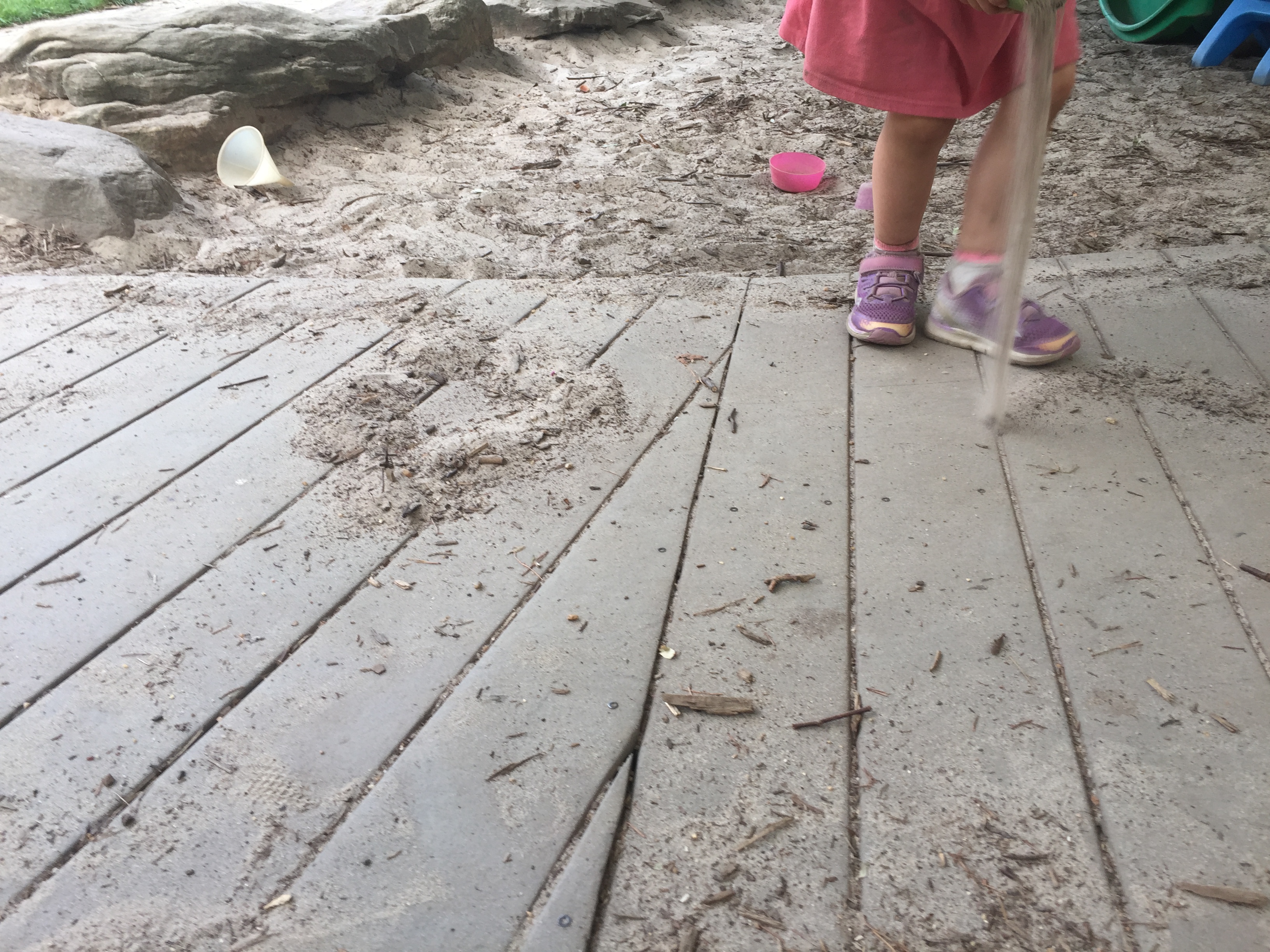Child pouring dry sand onto the walkway to create lines.