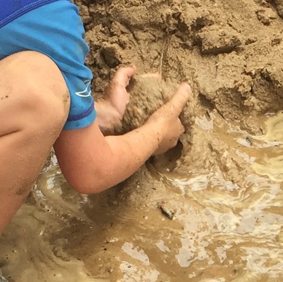 Child scooping up handfuls of wet sand.