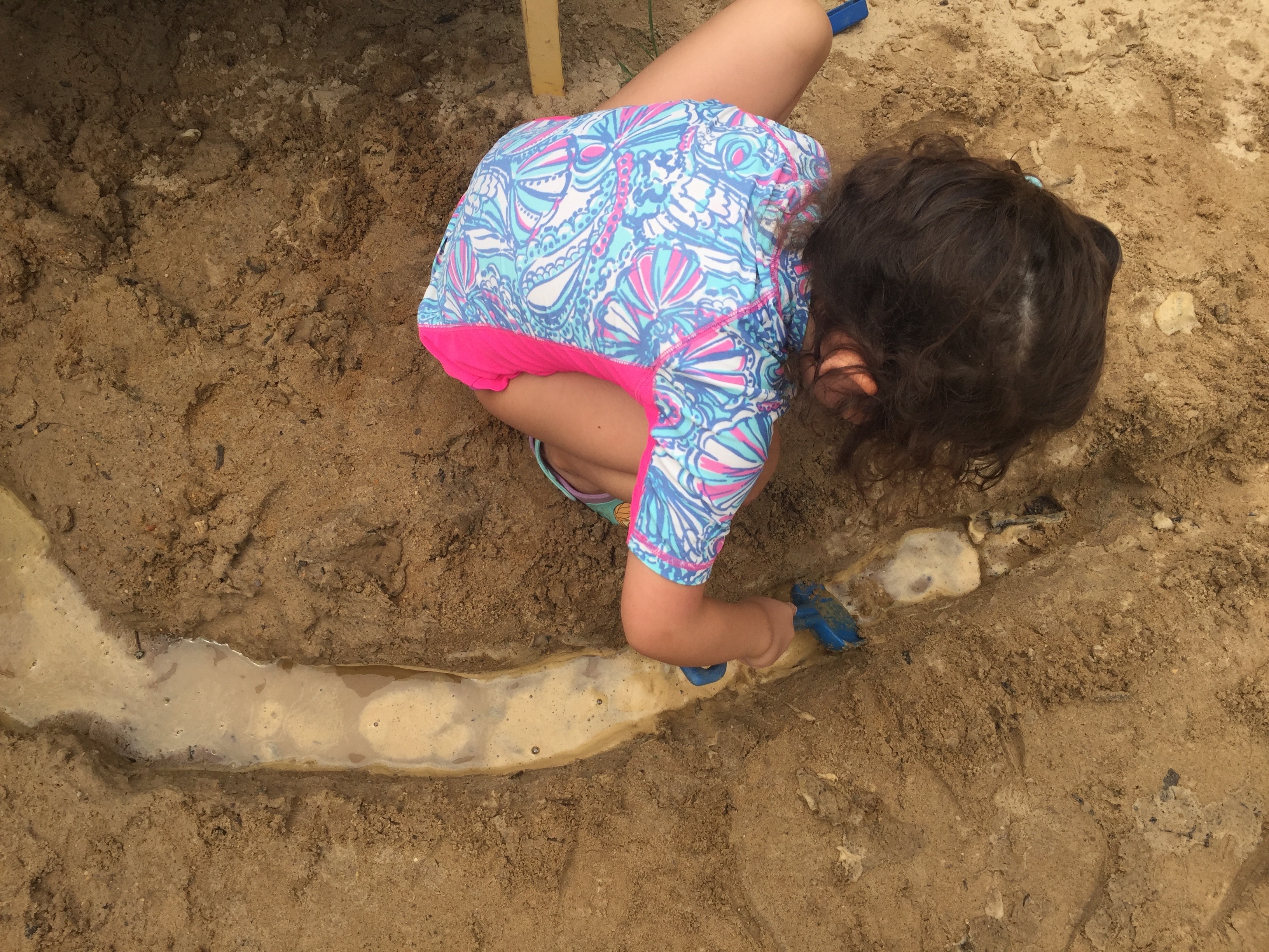 Child digging a channel for water in the sand.