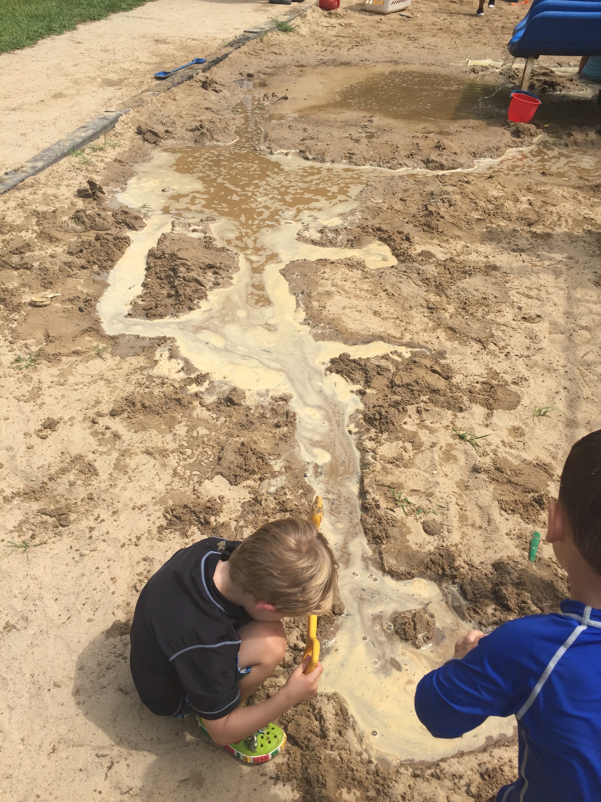 Two children digging a channel for water through a large expanse of sand.