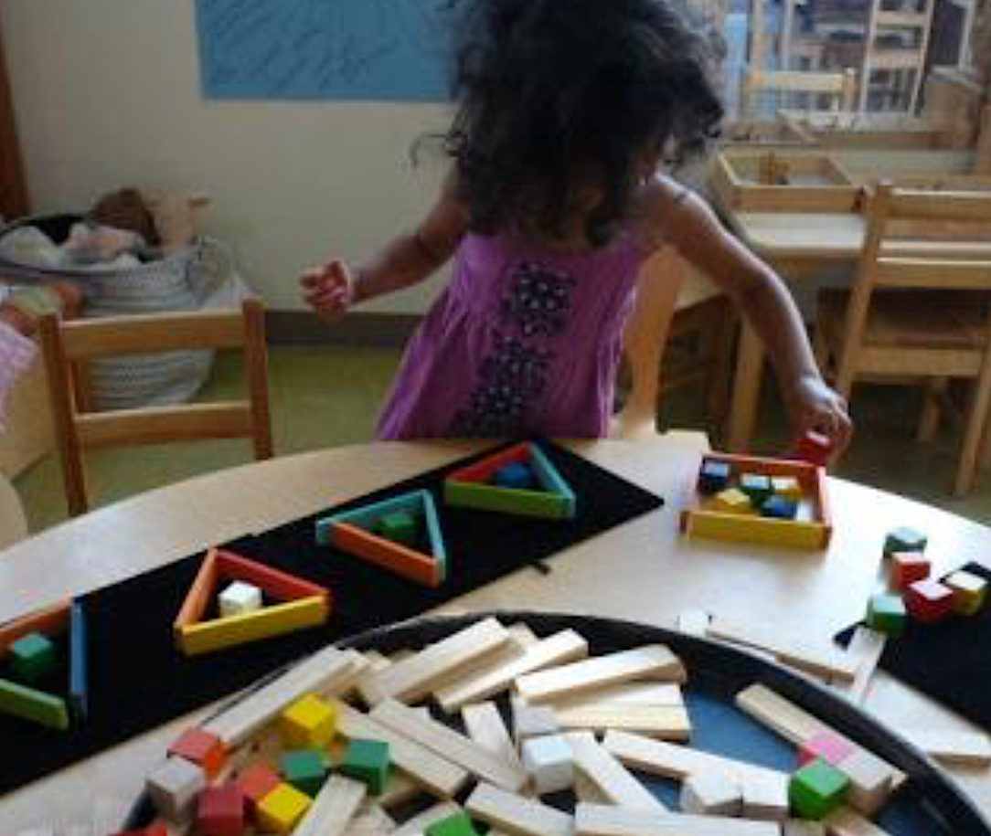Child arranges various blocks on a table indoors.