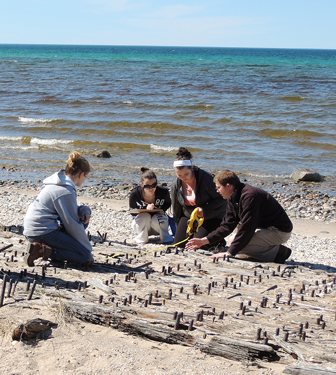 A teacher and students gather data for a county historical site and park, documenting cultural resources (shipwreck remains) exposed at the shoreline.