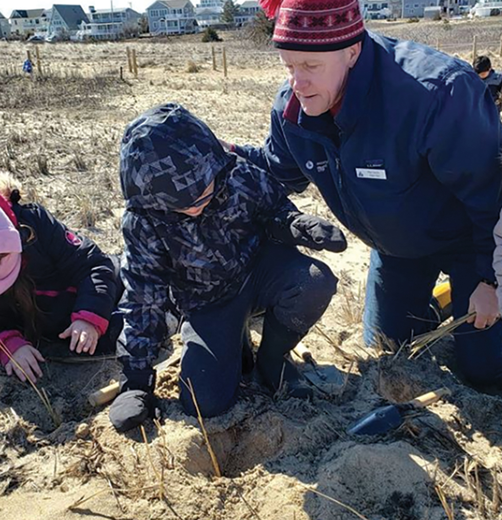 Students plant a dune grass plug with the support of a local volunteer.