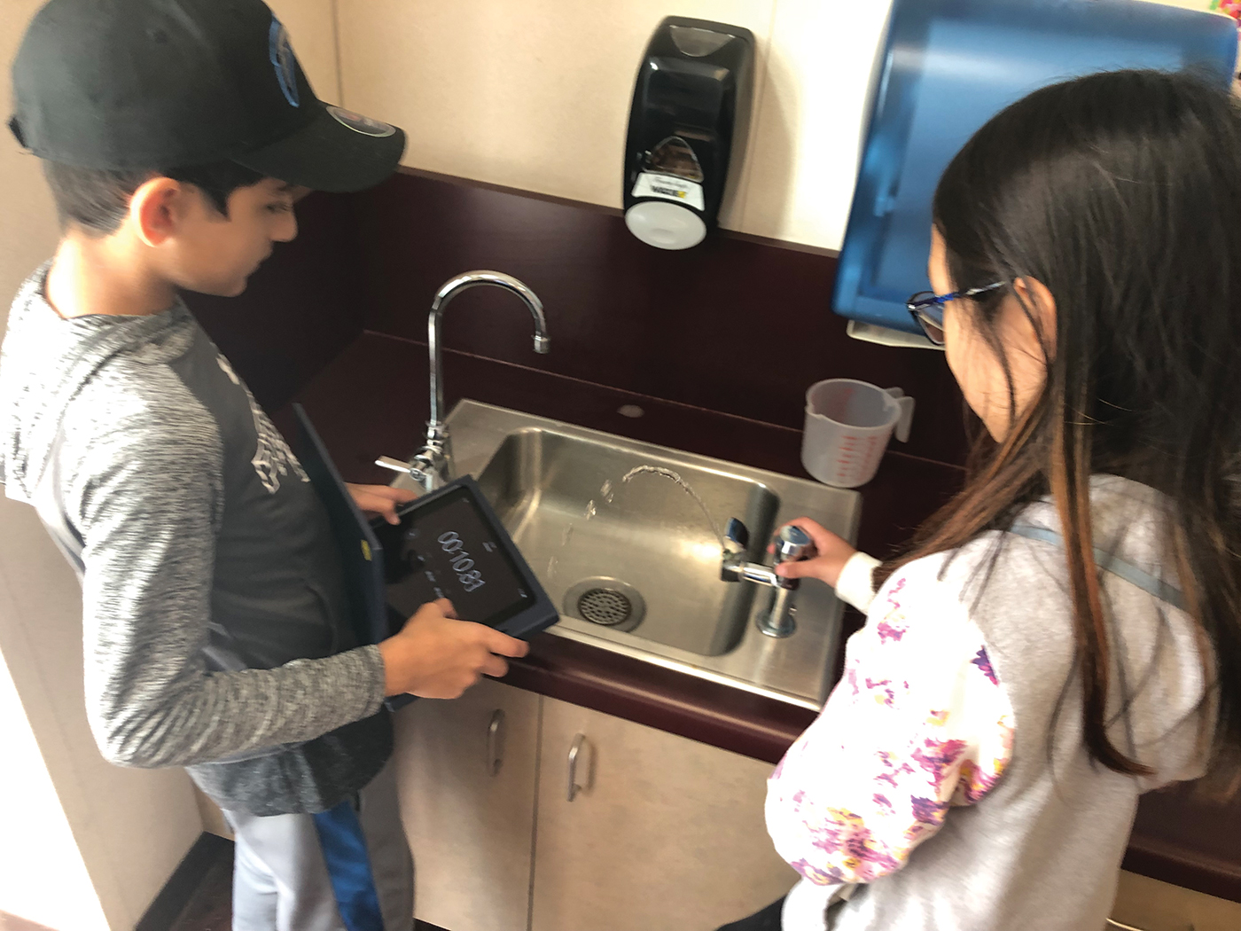 Students record the number of seconds the water continues to flow from a classroom water fountain after turning it off.