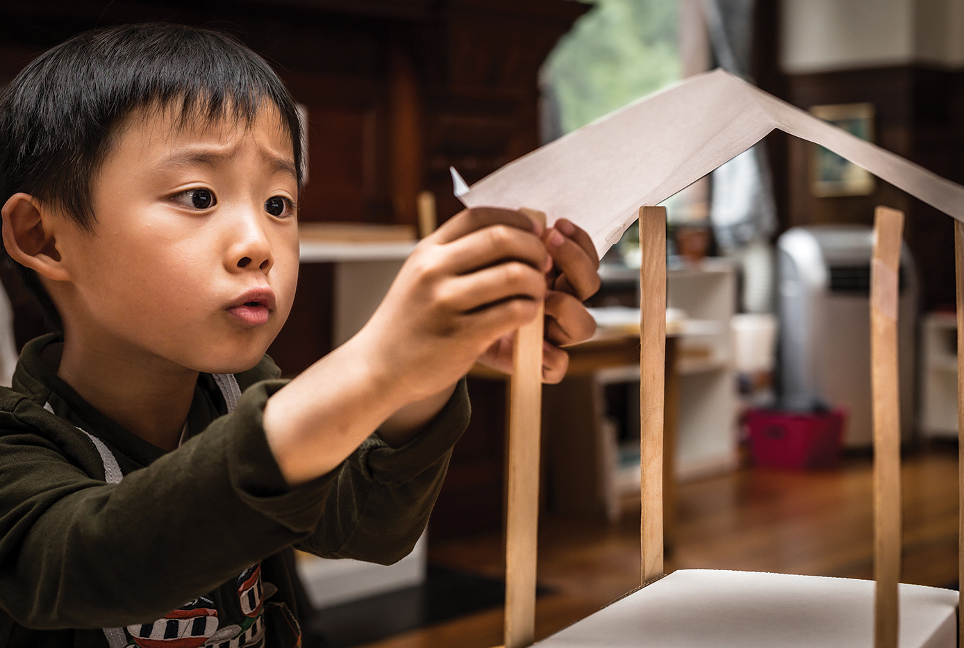 A student places a piece of paper roof on top of his dog shelter.