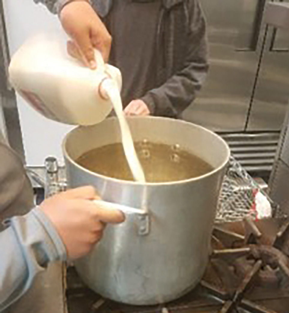 A Student Pours Milk into a pot for heating in the first step of the scaled-up kitchen procedure.
