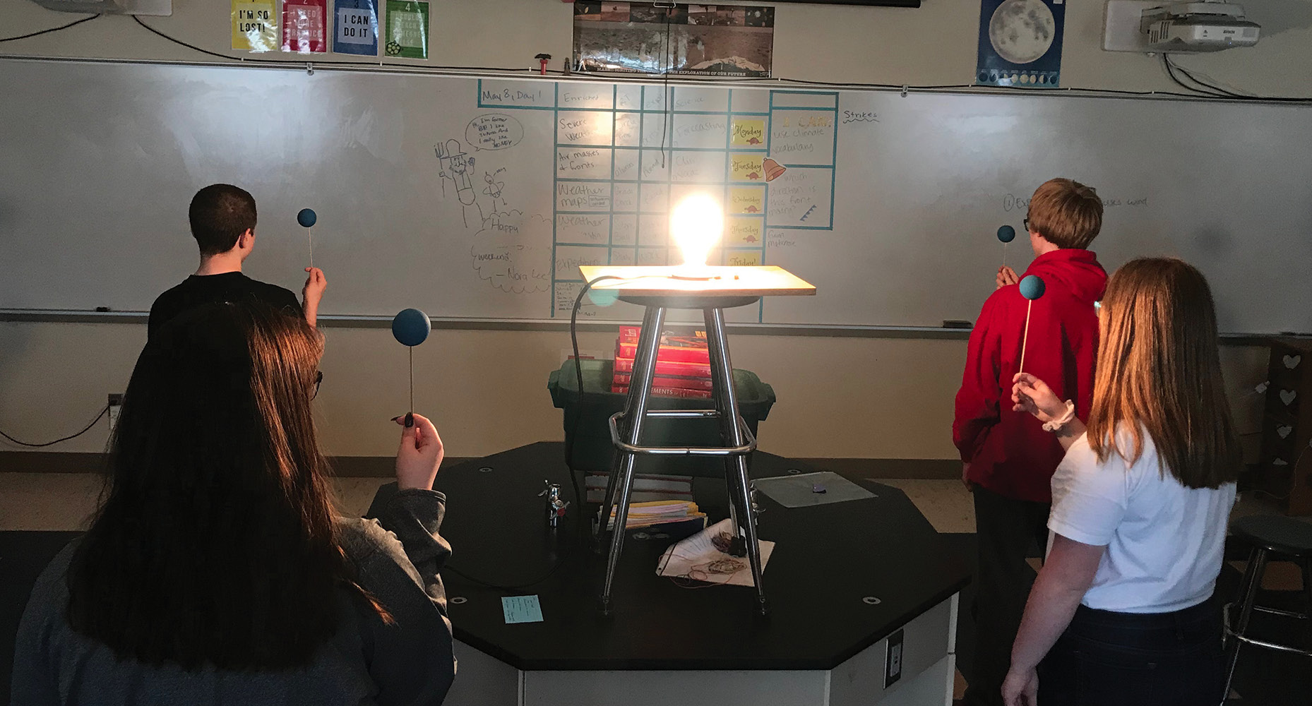 Figure 2 Students stand around the Sun (light bulb) with Moonballs facing different directions, resulting in students seeing different phases.