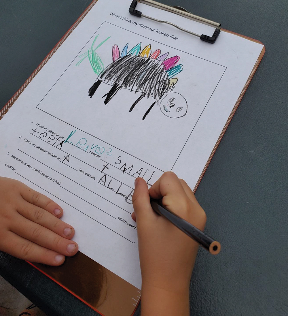 A student practices writing words while making inferences about her stegosaurus.